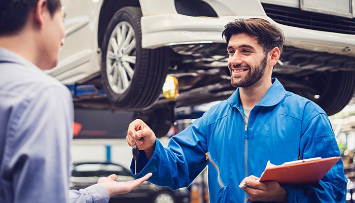 Mechanic handing car keys to customer under lifted vehicle